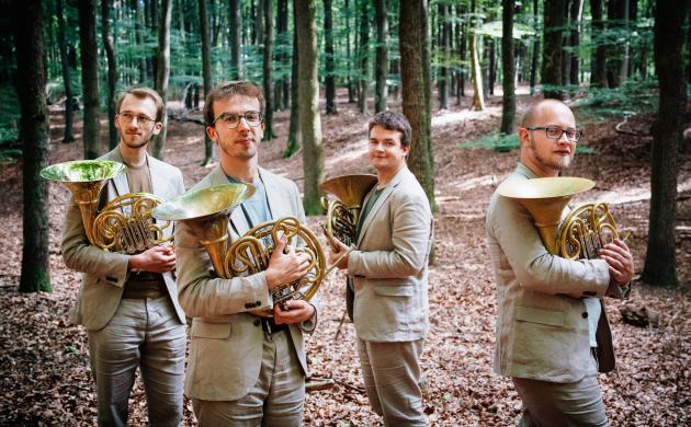 4 hoornisten van Korpus Kwartet in een bos met hun hoorn.